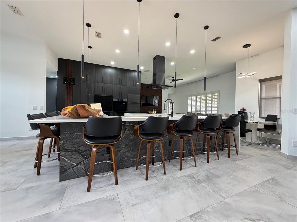 A modern kitchen features a large marble-topped island with bar stools and dark cabinetry — 4419 SADDLEWORTH CIRCLE, ORLANDO, FL