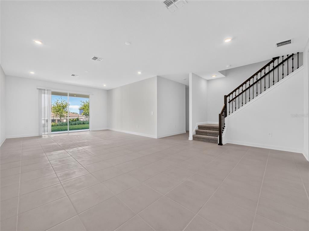 An open-concept living area features light tile flooring, white walls, and a carpeted staircase — 1283 DORA PARC LANE, MOUNT DORA, FL