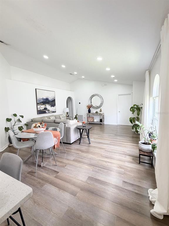 A bright living and dining area features light wood-look flooring, white walls, and vaulted ceilings — 409 TALQUIN COURT, ORLANDO, FL