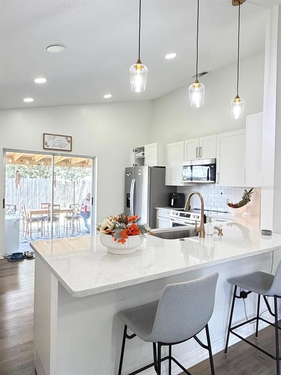 A modern kitchen features white cabinetry, quartz countertops, a breakfast bar, and pendant lighting — 409 TALQUIN COURT, ORLANDO, FL