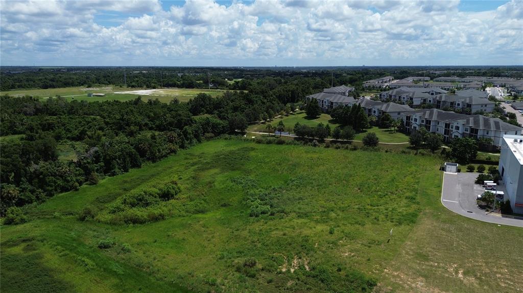 An aerial view shows a large, undeveloped grassy lot adjacent to an apartment complex — FOUNTAINS WEST BOULEVARD, OCOEE, FL