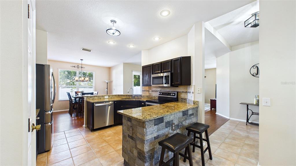 A kitchen with dark cabinets, granite countertops, a stone-faced breakfast bar, and tile flooring — 4021 3RD AVENUE E, BRADENTON, FL