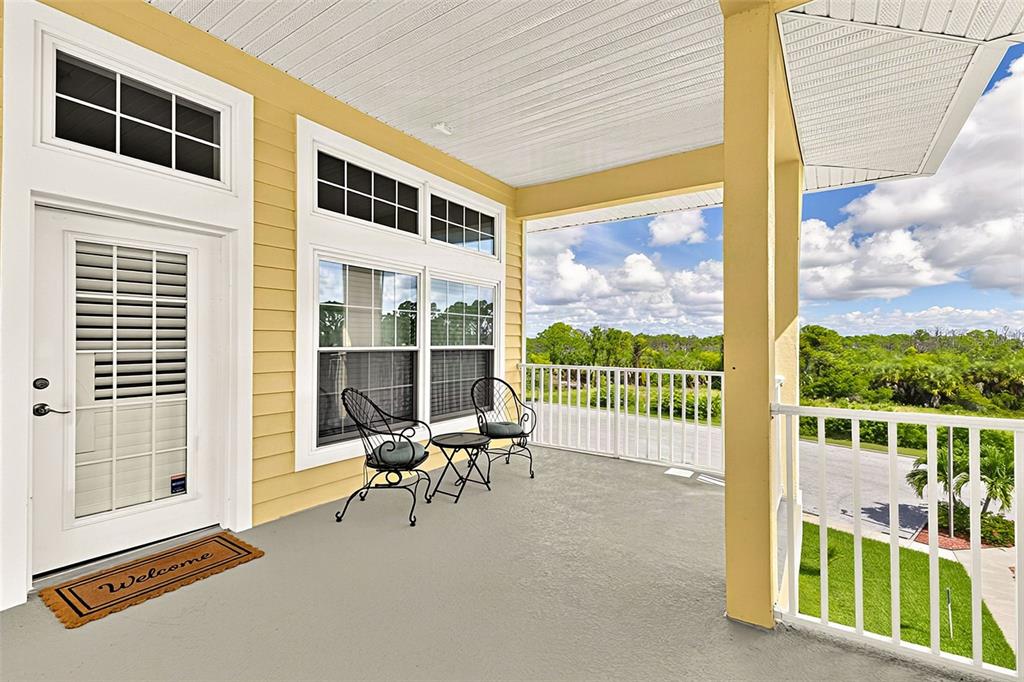 A covered porch with yellow siding, a white door, and two chairs overlooking a landscape — 101 NATURES WAY UNIT 1307, ROTONDA WEST, FL
