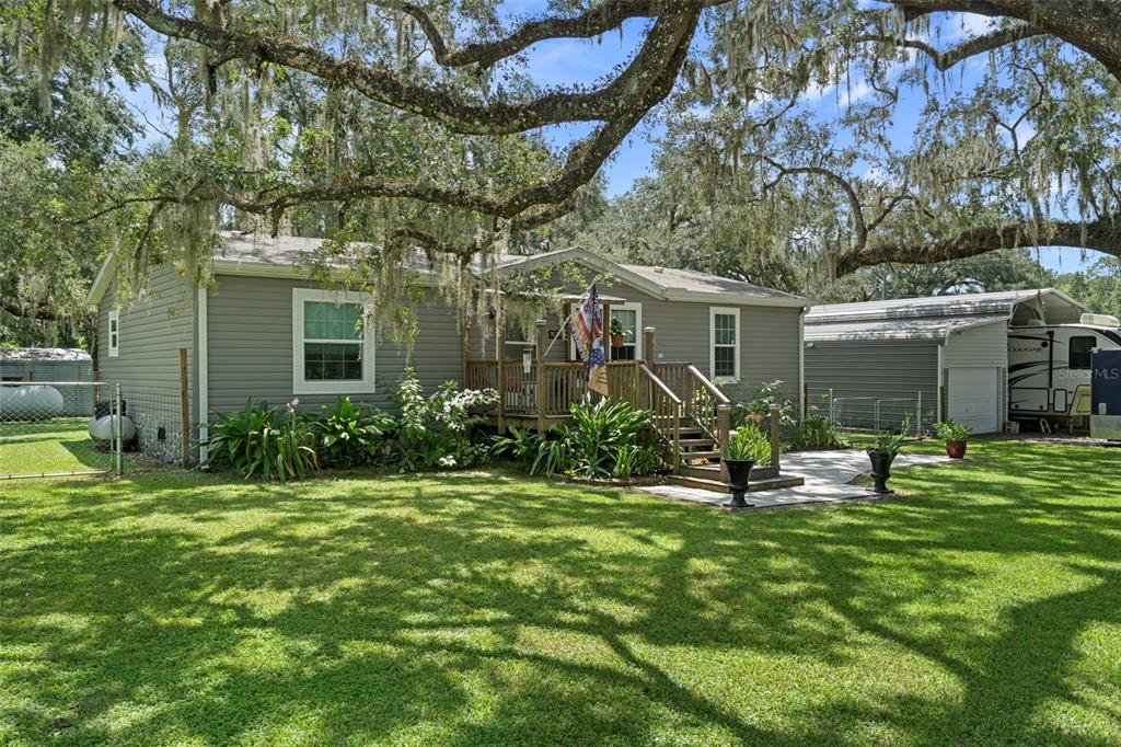 A gray single-story house with a wooden deck and a large lawn under oak trees — 9028 WEST STREET, BROOKSVILLE, FL