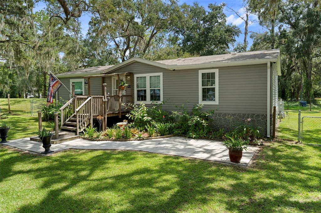 A single-story manufactured home with grey siding, a wooden front deck, and a stone patio — 9028 WEST STREET, BROOKSVILLE, FL