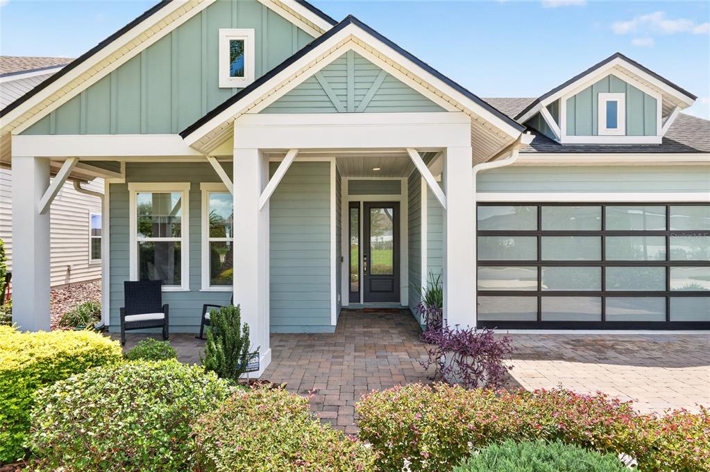 A single-story house exterior features light green siding, a covered porch, and a glass-paneled garage — 12027 SW 33RD PLACE, GAINESVILLE, FL