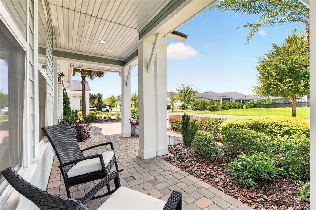 A covered front porch with stone pavers, two rocking chairs, and a view of landscaping — 12027 SW 33RD PLACE, GAINESVILLE, FL