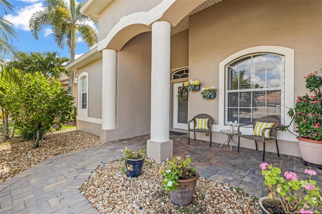 A paved walkway leads to a covered front porch with two chairs and potted plants — 2450 SILVER PALM ROAD, NORTH PORT, FL