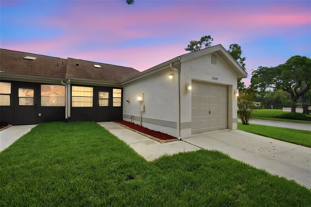 A single-story residential building with a white stucco exterior, a garage, and a grassy lawn — 11712 SPRING TREE LANE, PORT RICHEY, FL