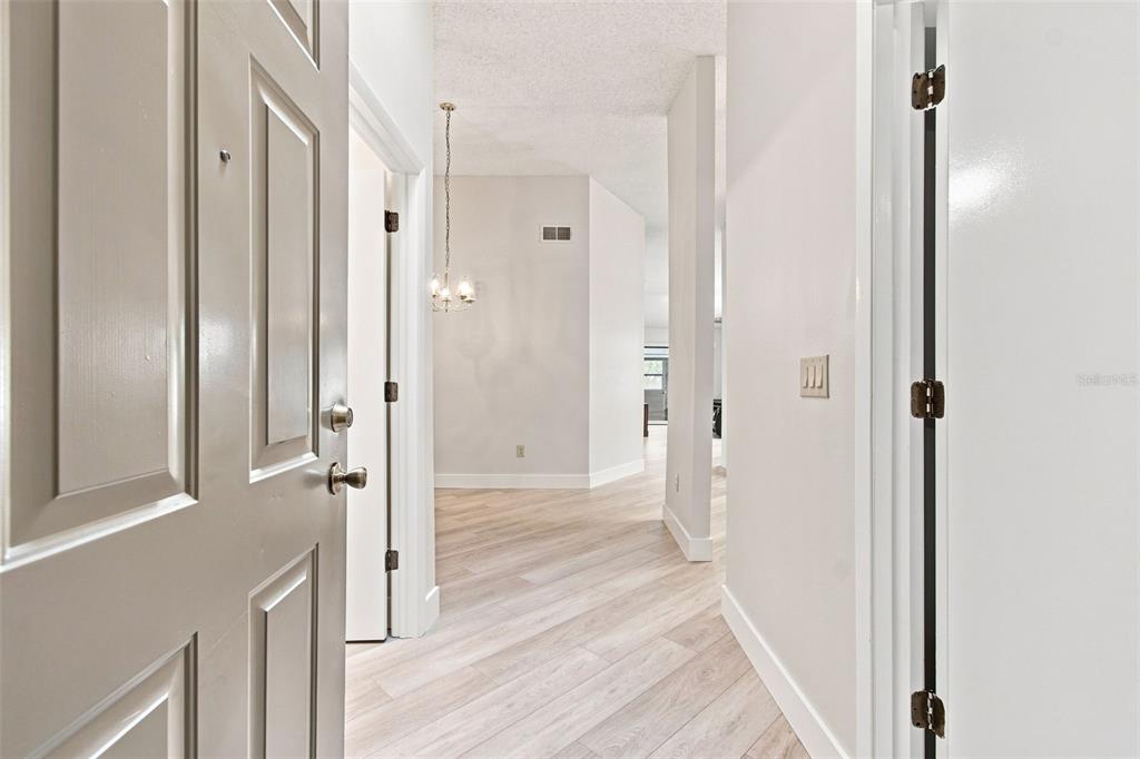 An entryway with light wood-look flooring leads into a hallway with a hanging light fixture — 11712 SPRING TREE LANE, PORT RICHEY, FL