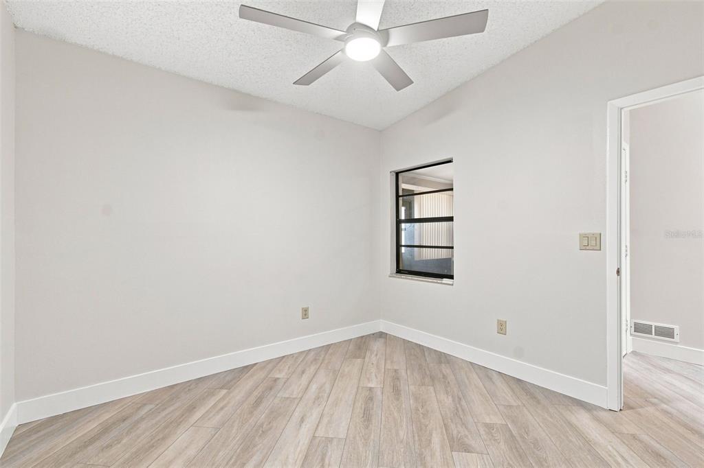A bedroom features a bed, a nightstand, a ceiling fan, and light-colored wood-look flooring — 11712 SPRING TREE LANE, PORT RICHEY, FL