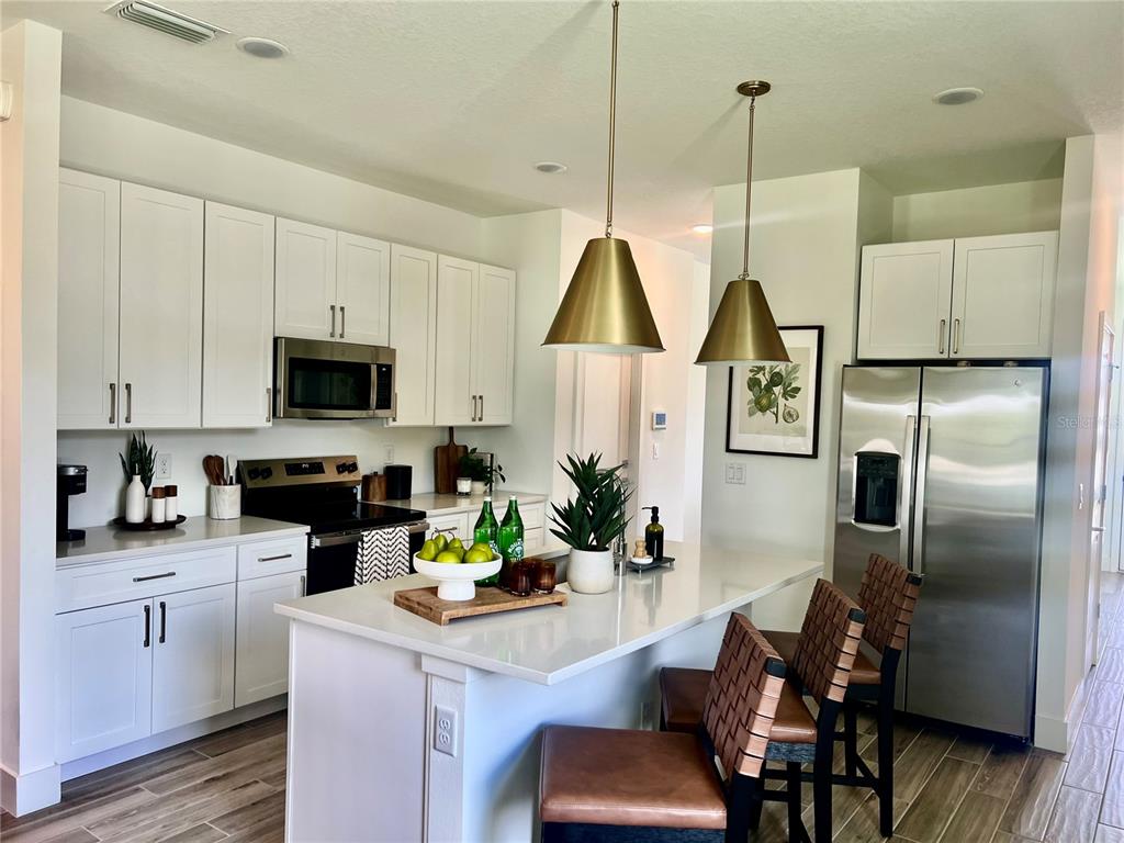A modern kitchen features white cabinets, stainless steel appliances, a quartz island, and two pendant lights — 101 ELENA LAVIN CIRCLE, ORLANDO, FL