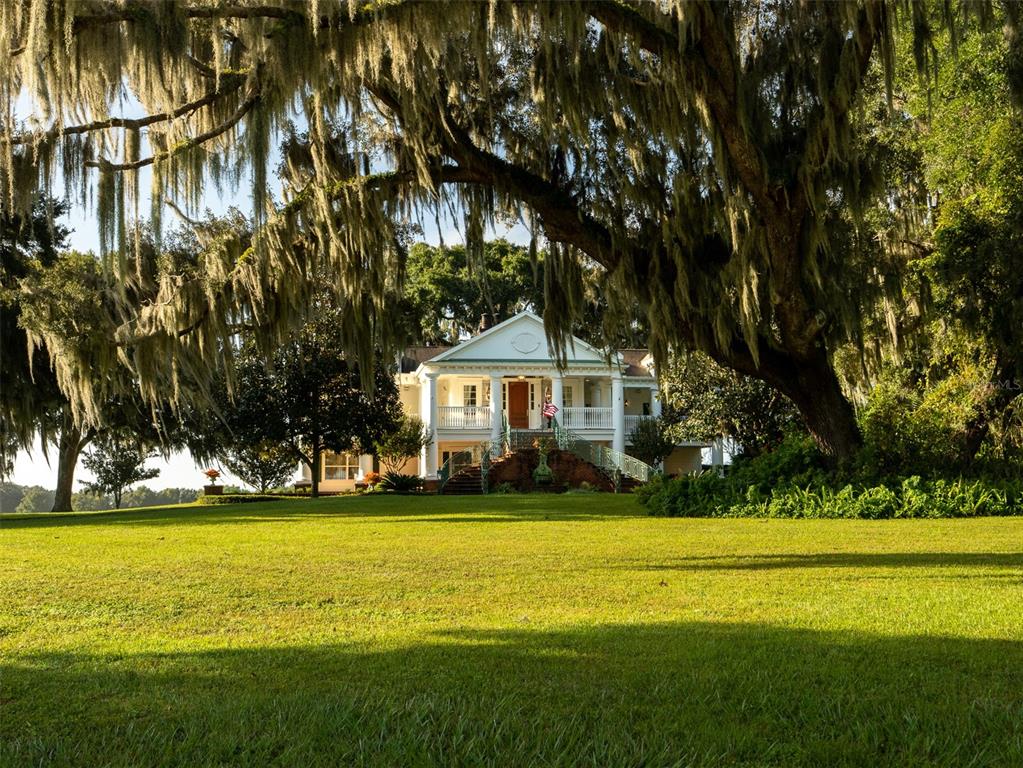 A white two-story colonial-style house sits behind a large lawn under moss-draped oak trees — 3682 W HIGHWAY 318, CITRA, FL