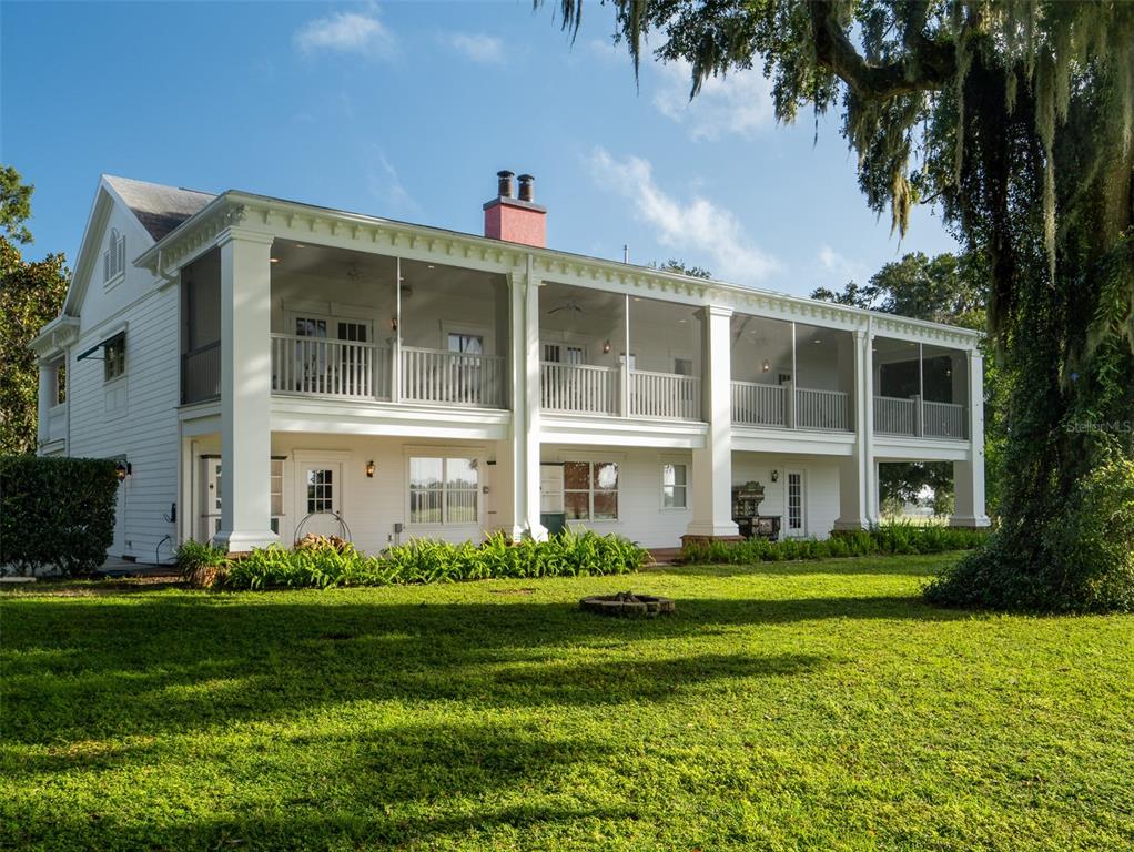 A two-story white house features a large screened-in porch and a chimney on the roof — 3682 W HIGHWAY 318, CITRA, FL