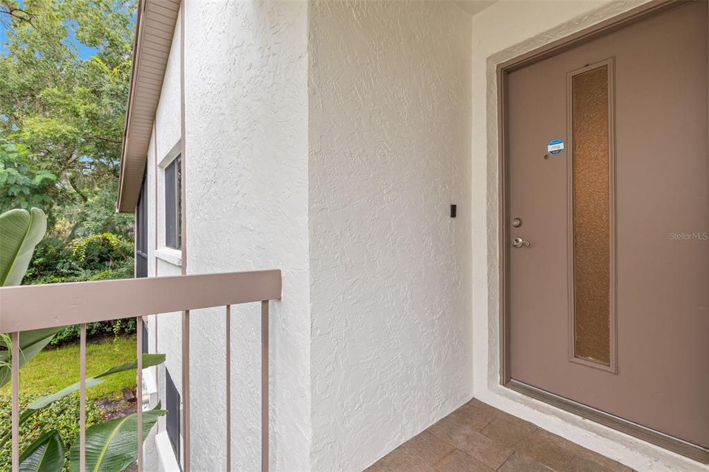 A tan front door with a vertical glass panel sits beside a white stucco wall — 631 FAIRMONT AVENUE UNIT C, SAFETY HARBOR, FL