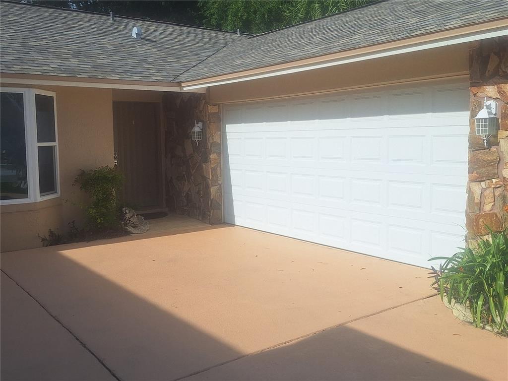 A tan house exterior features a white garage door, stone accents, and a concrete driveway — 9613 LEEWARD AVENUE, LARGO, FL