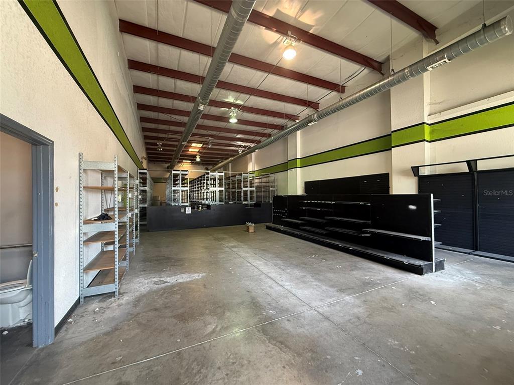 An industrial warehouse space features exposed ceiling beams, metal ductwork, and black retail shelving units — 5042 W HIGHWAY 40 UNIT 101, OCALA, FL