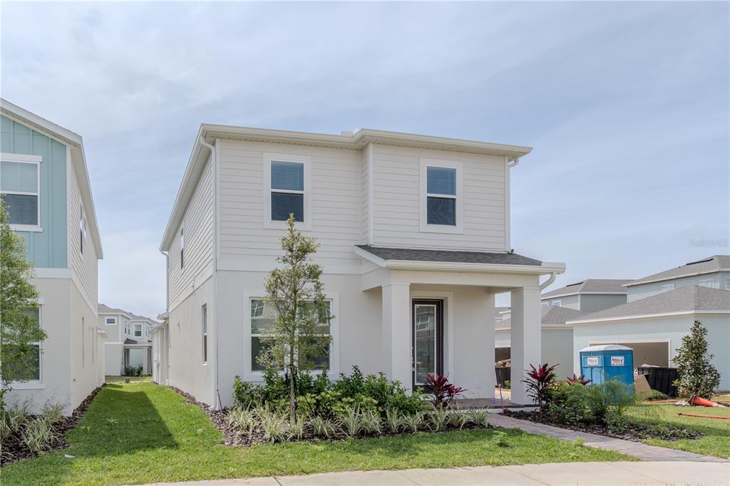 A two-story house with beige siding and a covered front porch under a cloudy sky — 16705 VICTORIA GROVE ALLEY, WINTER GARDEN, FL