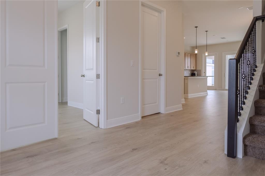 A hallway with light wood floors leads to a kitchen with a staircase on the right — 16705 VICTORIA GROVE ALLEY, WINTER GARDEN, FL