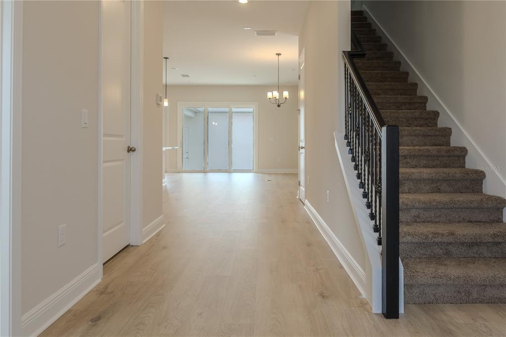 A bright entryway features light wood flooring, a carpeted staircase with a black railing, and doors — 16705 VICTORIA GROVE ALLEY, WINTER GARDEN, FL