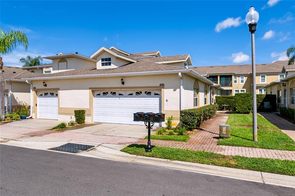 A brick walkway leads between two stucco buildings with manicured hedges and a small lawn — 17313 CHATEAU PINE WAY, CLERMONT, FL