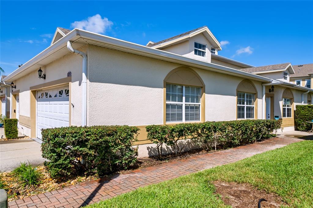 The exterior of a stucco home features a white door, arched windows, and a concrete patio — 17313 CHATEAU PINE WAY, CLERMONT, FL