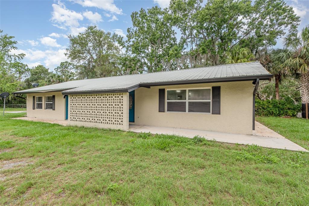 A single-story house with a metal roof, beige stucco walls, and a decorative breeze block screen — 4085 CYPRESS BEND, GENEVA, FL