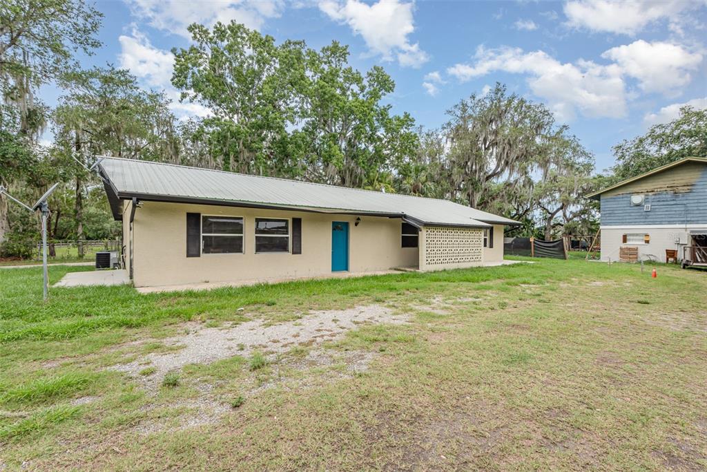 A single-story house with a metal roof, beige stucco walls, and a bright blue door — 4085 CYPRESS BEND, GENEVA, FL