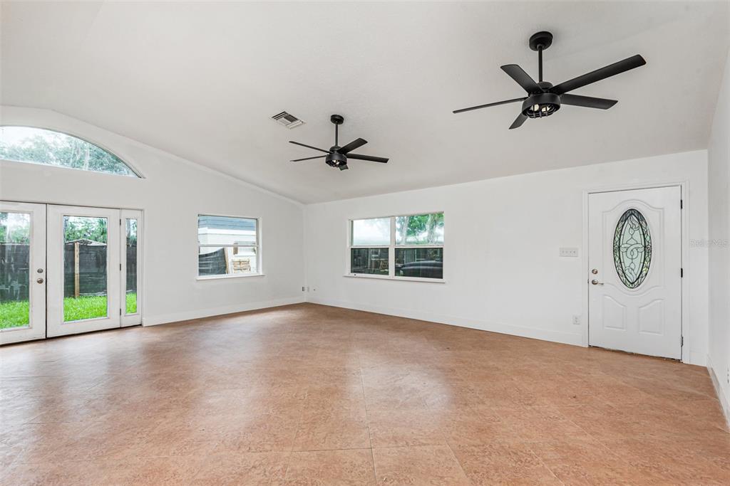 An empty living room features white walls, tile flooring, two ceiling fans, and a glass-paneled door — 4085 CYPRESS BEND, GENEVA, FL