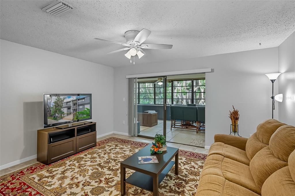 A living room features a tan sofa, a patterned area rug, and a sliding glass door — 2746 SW 14 DRIVE UNIT 2746, GAINESVILLE, FL