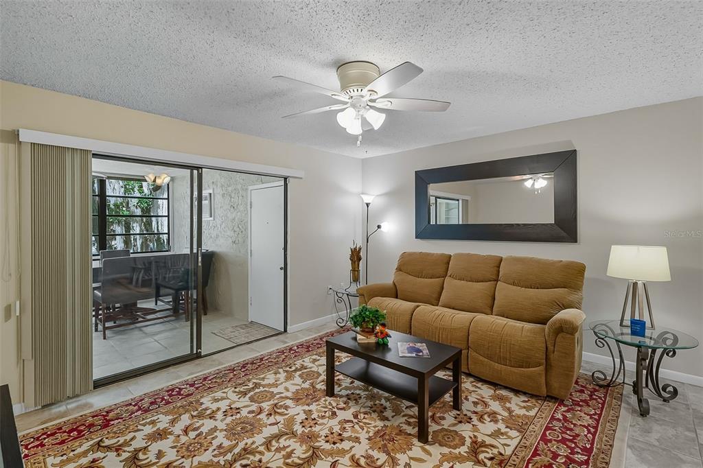 A living room features a tan sofa, patterned area rug, ceiling fan, and sliding glass doors — 2746 SW 14 DRIVE UNIT 2746, GAINESVILLE, FL