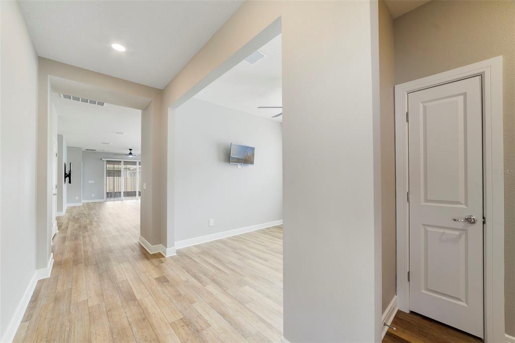 A hallway with light wood-look flooring leads to an open living area with a wall-mounted television — 2735 SUMMER RETREAT LANE, KISSIMMEE, FL
