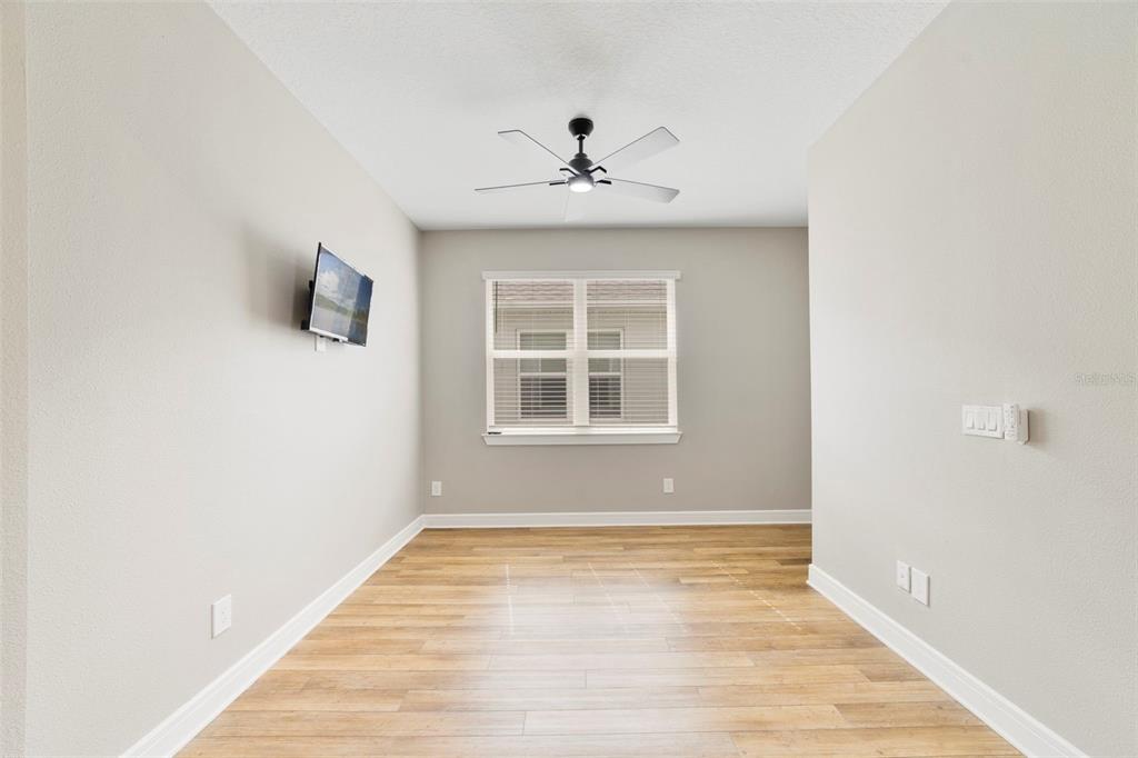 An empty room with light wood flooring, a ceiling fan, and a wall-mounted television — 2735 SUMMER RETREAT LANE, KISSIMMEE, FL