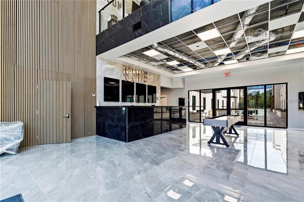 A modern lobby features a black marble reception desk, wood-slat walls, and a shuffleboard table — 4560 W IRLO BRONSON MEMORIAL HIGHWAY UNIT 203, KISSIMMEE, FL