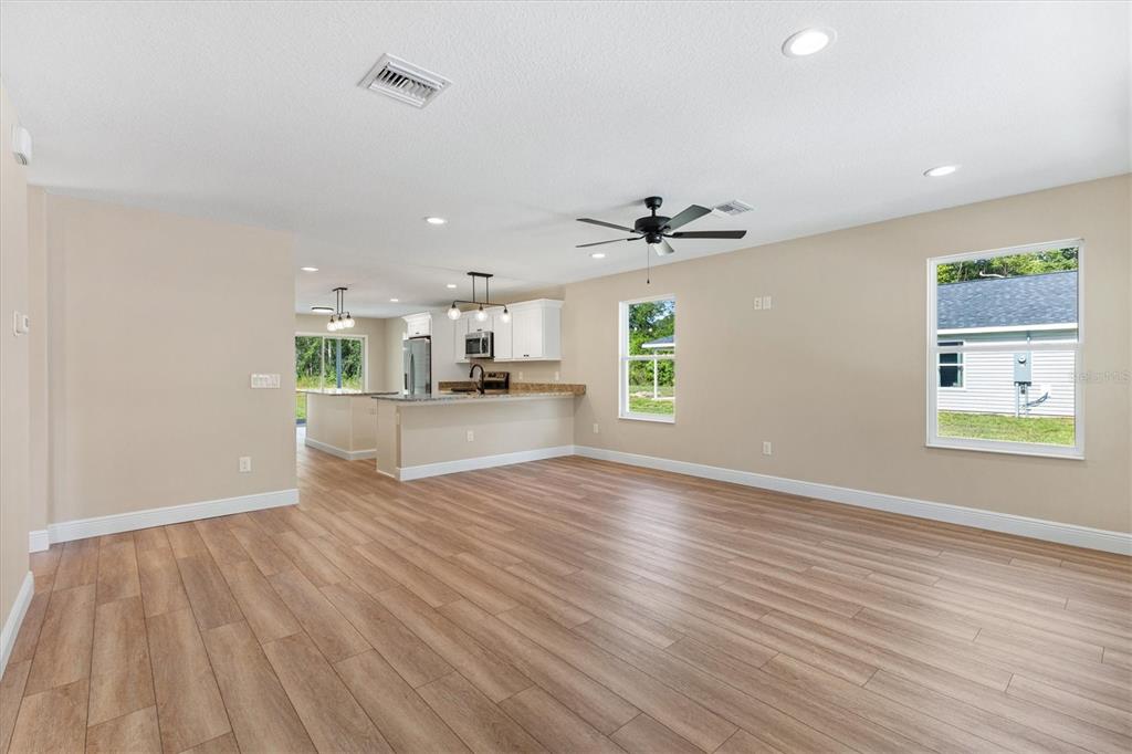 An open-concept living area features light wood-look flooring, beige walls, and a kitchen with white cabinets — 533 E ANDERSON AVENUE, BUSHNELL, FL