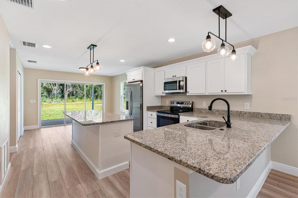 A kitchen features white cabinets, granite countertops, a center island, and a sliding glass door — 533 E ANDERSON AVENUE, BUSHNELL, FL