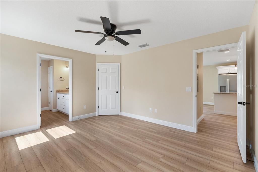 A bedroom with light wood-look flooring, a ceiling fan, and two doorways leading to other rooms — 533 E ANDERSON AVENUE, BUSHNELL, FL