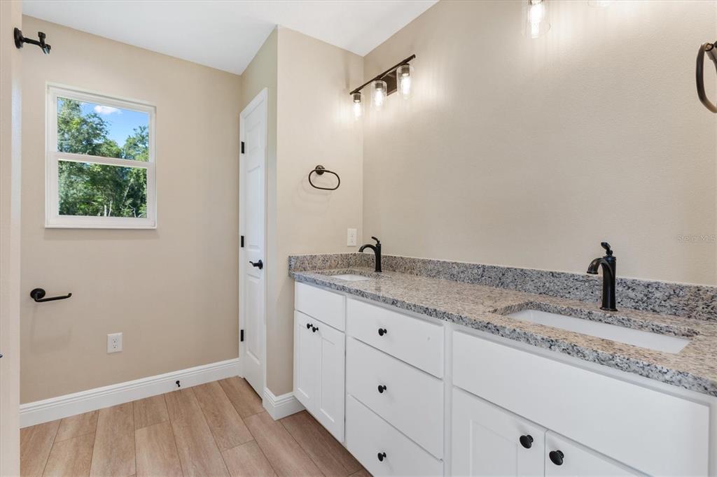 A bathroom features a double vanity with white cabinets, granite countertops, and wood-look flooring — 533 E ANDERSON AVENUE, BUSHNELL, FL