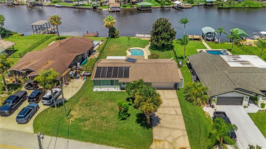 An aerial view shows a waterfront house with a pool, solar panels, and a driveway — 988 SHOCKNEY DRIVE, ORMOND BEACH, FL