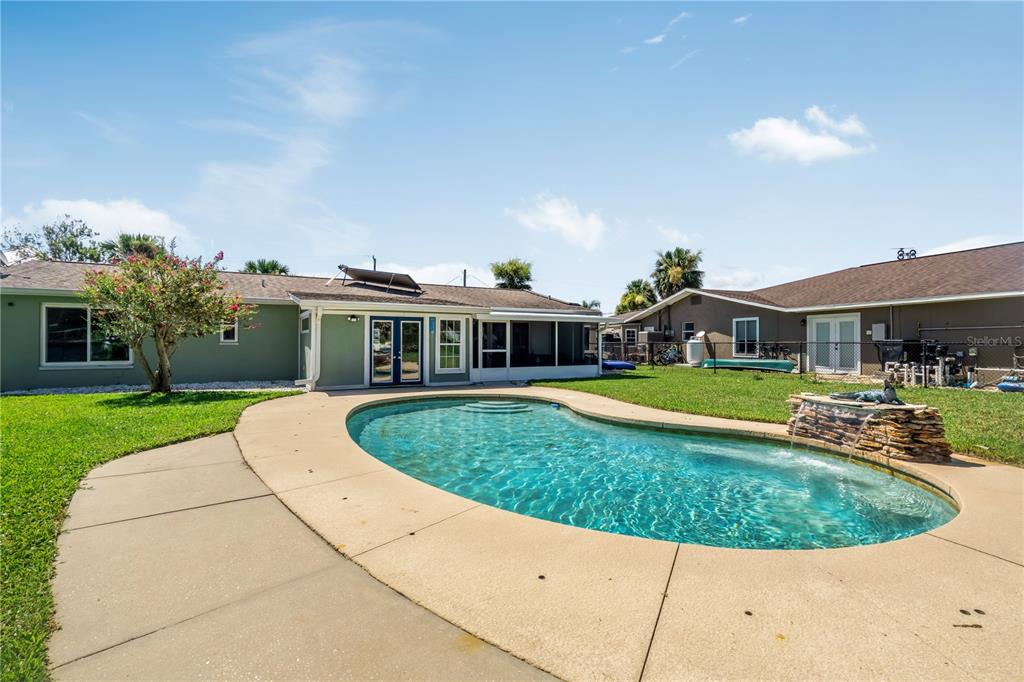 A backyard features a kidney-shaped swimming pool with a stone waterfall and a concrete patio — 988 SHOCKNEY DRIVE, ORMOND BEACH, FL