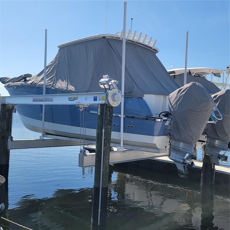 A blue motorboat with a gray cover sits on a boat lift over water — 312 11TH AVENUE E, PALMETTO, FL