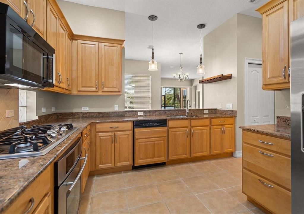 A kitchen features light wood cabinets, granite countertops, stainless steel appliances, and tile flooring — 312 11TH AVENUE E, PALMETTO, FL
