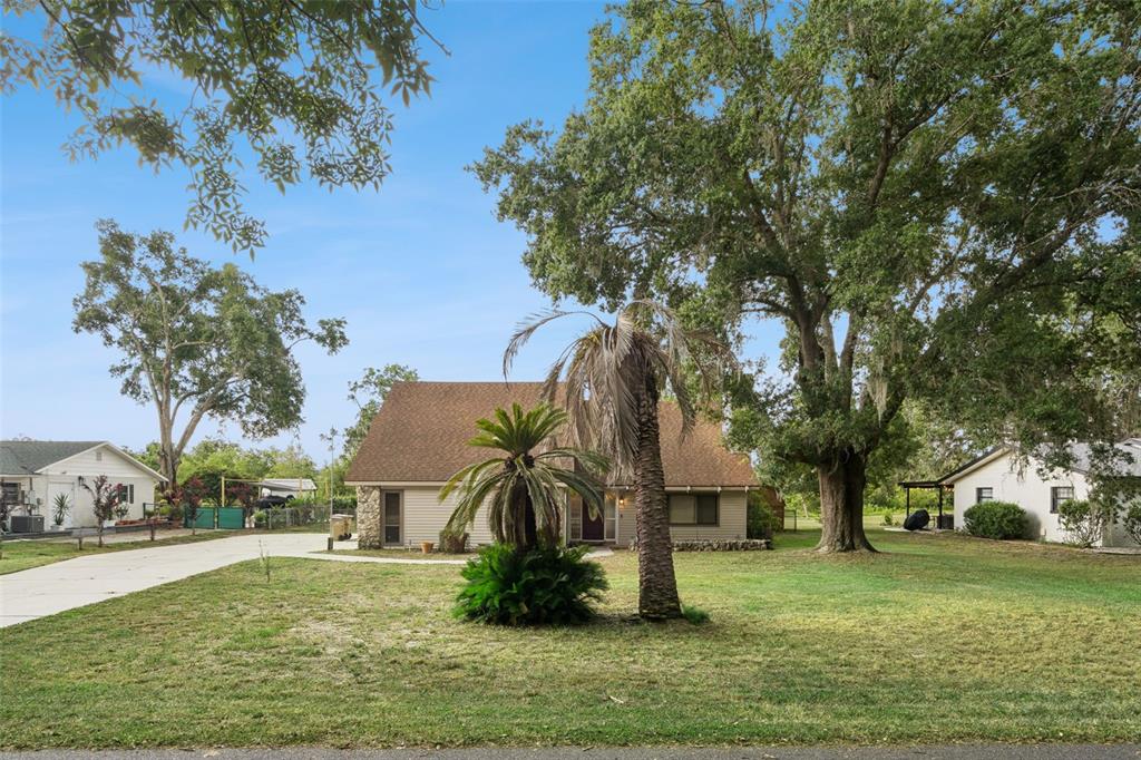 A single-story house with a brown roof sits on a grassy lot with large trees — 9916 JACKSON ROAD, LEESBURG, FL