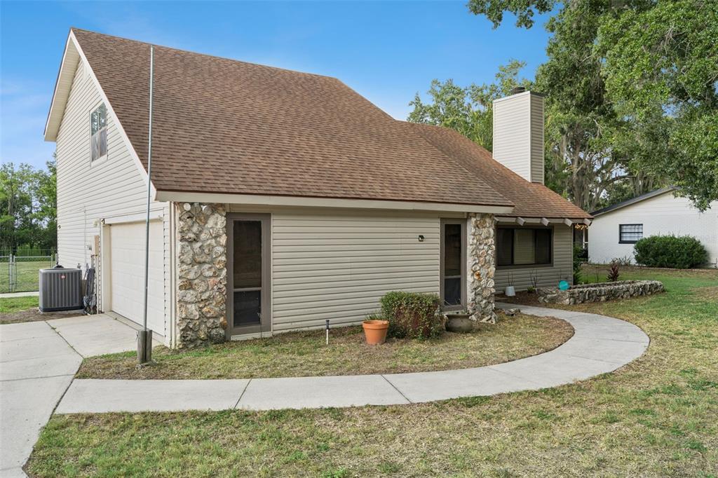 A beige house with stone accents, a brown shingled roof, and a curved concrete walkway — 9916 JACKSON ROAD, LEESBURG, FL