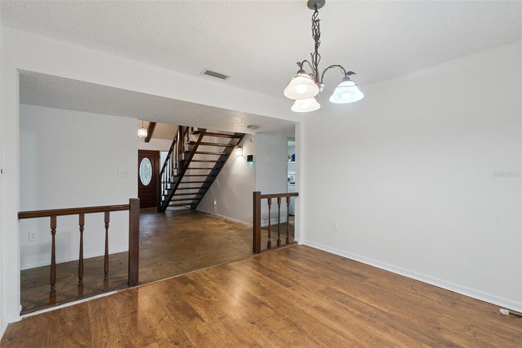 A dining area with wood-look flooring leads to an entryway with a staircase and railing — 9916 JACKSON ROAD, LEESBURG, FL