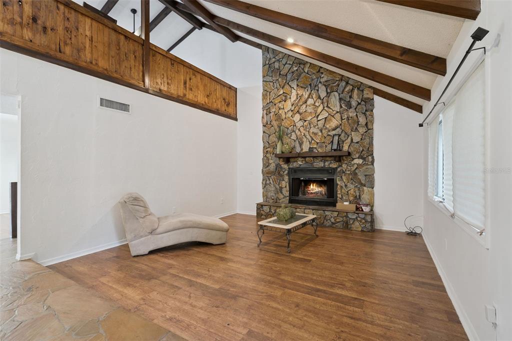 A living room features a stone fireplace, vaulted ceiling with exposed beams, and wood flooring — 9916 JACKSON ROAD, LEESBURG, FL