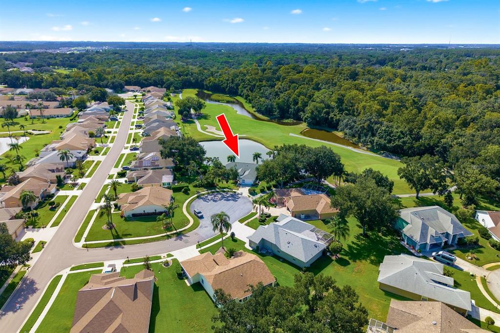 An aerial view shows a suburban neighborhood with houses surrounding a pond and golf course — 6639 SUN POINT COURT, NEW PORT RICHEY, FL