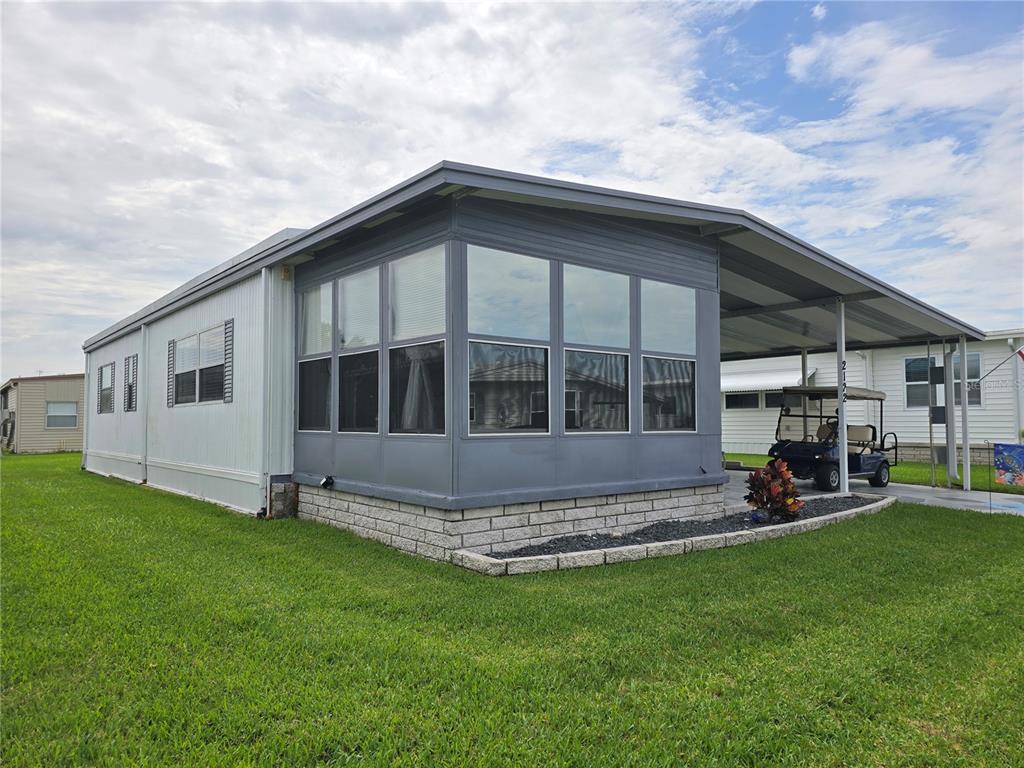 A manufactured home with a glass-enclosed sunroom, a metal carport, and a golf cart parked underneath — 2122 WATERVIEW DRIVE, HOLIDAY, FL