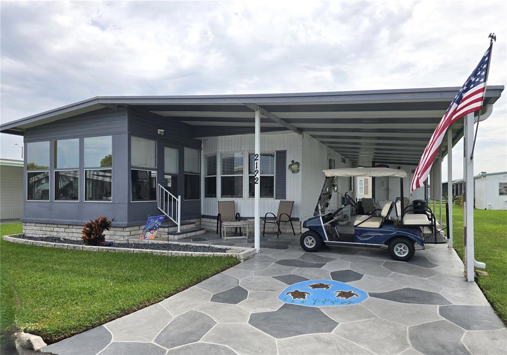 A manufactured home with a carport, decorative concrete driveway, and an American flag — 2122 WATERVIEW DRIVE, HOLIDAY, FL