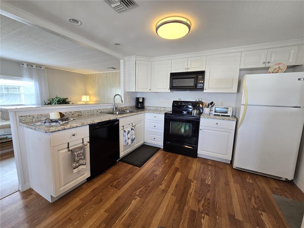 A kitchen features white cabinets, black appliances, granite countertops, and wood-look flooring — 2122 WATERVIEW DRIVE, HOLIDAY, FL